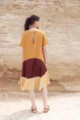 Vestido corto color mostaza con corte evasé y mangas cortas. Presenta un bloque de color marrón en la falda y otro bloque color beige en el ruedo.