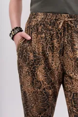 Pantalón babucha de tiro medio, ajustado en tobillos, con estampado de piel de serpiente en tonos marrones y negros. Posee bolsillos diagonales y cintura elastizada con cordón de ajuste.