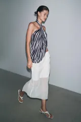 Falda midi color blanco, semitransparente, de tiro medio con cintura elástica, forro corto interior y abertura en la espalda.