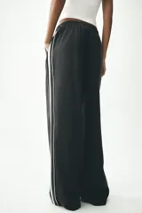 Pantalón negro de tiro alto con cintura elástica, bolsillos delanteros y detalle de banda lateral blanca.