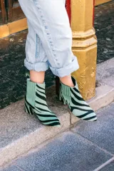 Botines de cuero con estampado de cebra en tonos verde claro y negro, con puntera fina y tacón cuadrado. Presentan paneles laterales elásticos en color verde liso.