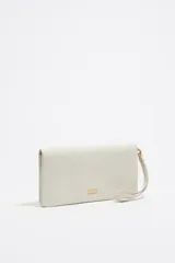 Billetera de cuero sintético color blanco con textura granulada. Tiene cierre con solapa y botón a presión, múltiples compartimentos internos para tarjetas y billetes, y un bolsillo con cierre para monedas. Incluye una correa de mano extraíble.