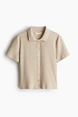 Remera polo color beige, entallada, de punto acanalado suave, con mangas cortas, cuello clásico y tapeta con botones nacarados.