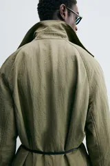 Trench color verde oliva de tejido técnico, corte relaxed fit, cuello solapa, manga larga, bolsillos laterales y abertura en la espalda.