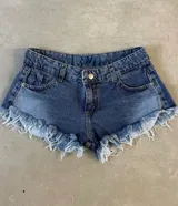 Short de jean azul con tiro alto, bolsillos delanteros y traseros, y ruedo desflecado.