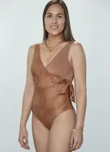 Traje de baño entero color cobre con estampado de flores y hojas en tonos dorados. Diseño cruzado con escote en V y lazo lateral.