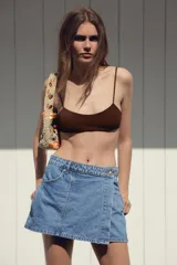 Minifalda pantalón de tiro alto confeccionada en denim celeste, con bolsillos delanteros y traseros. Presenta cierre frontal cruzado con cremallera oculta y botón metálico.