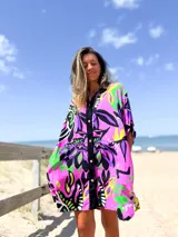 Camisero de manga corta, corte holgado, con cuello camisero y botones frontales. Presenta un estampado vibrante de motivos florales en tonos fucsia, negro, lila, verde lima y amarillo.