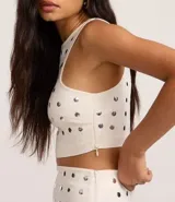 Top cropped sin mangas, color blanco, con escote redondo y tachuelas metalizadas distribuidas por toda la prenda. Posee cierre lateral de cremallera.