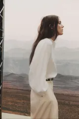 Blusa blanca de corte holgado en tejido liviano de lino y viscosa con canesú delantero en broderie. Cuello mao con frunces en la nuca, botones forrados adelante y mangas globo largas con puños finos abotonados. Bajo redondeado.