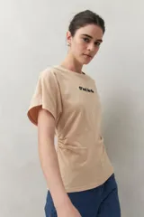 Remera blanca de manga corta con bordado frontal "C’est la vie", calce relajado y frunces laterales.