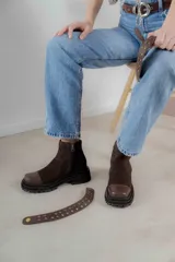 Bota corta de cuero gamuzado color marrón chocolate, con punta cuadrada y suela track. Presenta una correa con hebilla desmontable y cierre lateral con cremallera.