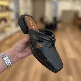 Zueco de cuero negro con taco bajo y detalle de nudo en el empeine.