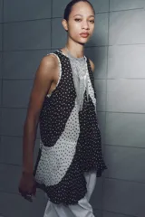 Top de cuello redondo y manga sisa con detalle de tejido plisado semitransparente y estampado de lunares blancos y negros. Bajo asimétrico y cierre en espalda con abertura y botón.