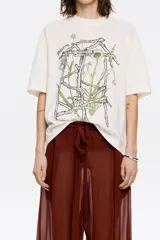 Remera negra de algodón con cuello redondo y manga corta. Estampado frontal con diseño floral abstracto en tonos rosa y marrón.