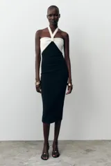 Vestido midi negro de tejido elástico, con escote recto y cuello halter. Presenta un lazo blanco a contraste en el delantero con aplicación de perlas y espalda descubierta.