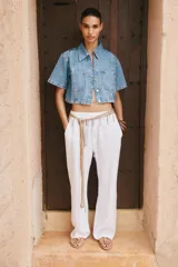 Camisa de denim celeste de corte crop, con cuello solapa, escote en pico, manga corta y dos bolsillos delanteros con botón. Cierre frontal con botones metálicos.
