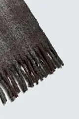 Bufanda rectangular con estampado de cuadros en tonos grises y negros, con acabado cepillado y flecos en los extremos.