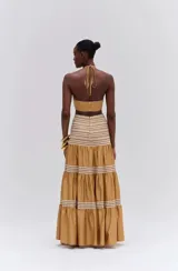 Vestido largo color ocre sin mangas, confeccionado en tricolina con forro. Presenta bordados en madera, hilo y pedrería, abertura en la cintura y tira para atar al cuello.