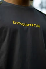 Remera gris oscuro de manga corta raglán, confeccionada en algodón. Presenta costuras a la vista en color amarillo.