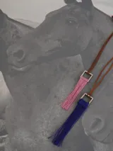 Collar con cordón de cuero marrón y dije cuadrado de metal con flecos rojos.