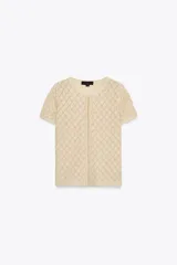 Top color crema de tejido de punto calado con patrón de rombos, cuello redondo, manga corta y cierre frontal con ganchos metálicos.