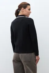 Chaqueta de tejido color terracota/lacre, con cuello y bordes de bolsillo en blanco con textura de punto. Posee cierre frontal de botones y manga larga.