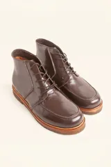 Bota de cuero vacuno con acabado charol, color marrón oscuro. Presenta un diseño de caña corta con cordones frontales y costuras decorativas en la puntera. La suela es de goma tipo crepe.