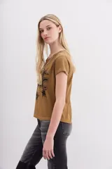 Remera color camel de mangas cortas confeccionada en jersey de algodón, de calce al cuerpo y escote redondo en punto rib a tono. Cuenta con una estampa central al agua de efecto desgastado con la palabra "Music" y estrellas, y un aplique de cadenas y piedras que simula ser un collar.