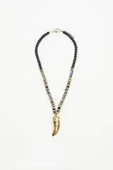 Collar largo con cadena compuesta por cuentas de madera pintada en negro y blanco, cuentas metálicas doradas y cuentas ovaladas negras. Dije central metálico dorado con forma de cuerno con texturas.