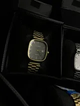 Reloj Casio Quartz dorado con caja cuadrada, dial negro y pulsera de eslabones.