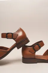 Zapato marrón de cuero con correa al tobillo y hebilla negra. Diseño trenzado en la parte delantera.