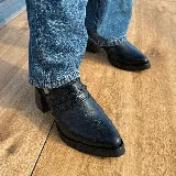 Zuecos negros de cuero con punta fina, taco cuadrado y tira trasera con hebilla. Presentan detalle de trenzado en el empeine.