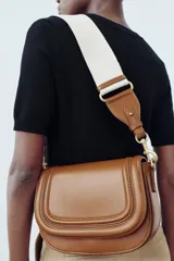 Bolso bandolera color marrón con solapa y correa ancha de tela color crudo.