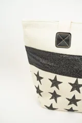 Bolso tipo tote con estampado de estrellas negras sobre fondo beige y una franja horizontal negra con glitter.