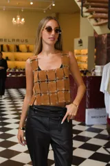 Top corto sin mangas de gamuza color camel, compuesto por paneles rectangulares unidos por ojales metálicos plateados.