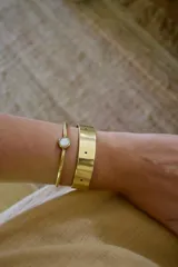 Pulsera rígida dorada con una piedra redonda de nácar en el centro.