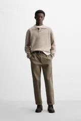 Sweater color beige de punto canalé con cuello polo, solapas amplias y cierre frontal con dos botones.