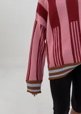 Sweater de punto oversize a rayas verticales rosas y bordó, con cuello alto y puños con ribete celeste.