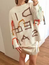 Sweater tejido de algodón color crudo, con bordados de letras en marrón, naranja, rojo, verde y celeste. Diseño oversize con flecos de hilo en las mangas.