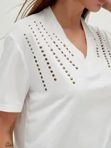 Remera negra de corte holgado con cuello en V y apliques de tachas doradas en los hombros.