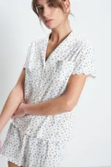 Conjunto de pijama corto de algodón blanco con estampado de pequeñas flores azules. Incluye camisa de manga corta con cuello y botones, y short con cintura elástica y volados en el ruedo.