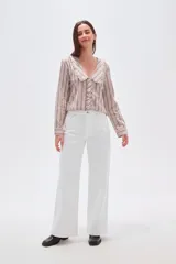 Camisa de algodón con estampado de rayas verticales en tonos beige y marrón. Presenta un cuello solapa con detalle de volados, cierre frontal con botones y mangas largas.
