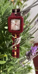 Reloj de pulsera con caja cuadrada y correa de eslabones de madera color borgoña. El dial es plateado con agujas y detalles dorados.