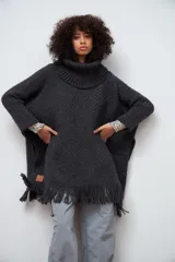 Poncho tejido de lana color gris oscuro, con cuello alto y flecos en el ruedo.