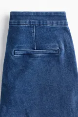 Jean de tiro alto con corte acampanado desde la rodilla. Confeccionado en denim con leve stretch, presenta cierre frontal con botón oculto y corchete, bolsillos traseros decorativos y pliegues frontales y posteriores.