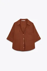 Camisa de lino color celeste claro, con cuello solapa, escote pico, manga corta con vuelta y dos bolsillos de plastrón en el delantero. Cierre frontal con botones.