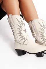 Botas tejanas off white de cuero, con diseño de costura en la caña y tacón de 4 cm, cierre lateral.