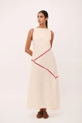 Vestido largo de lino color crudo con cuello semi-bote y tajos laterales. Presenta vivos de color fucsia que delinean el escote, sisas y recorren el cuerpo en líneas diagonales asimétricas.