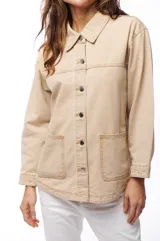 Sobrecamisa de jean color beige, con cuello clásico, cierre frontal con botones y dos bolsillos de parche en el pecho.